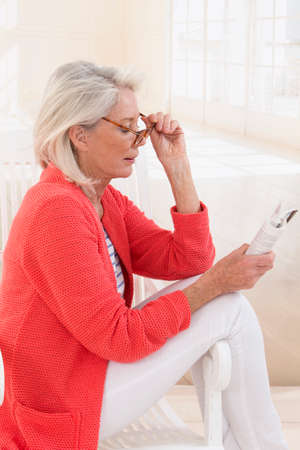 Senior Woman Relaxing In Chair At Home Reading Bookの写真素材