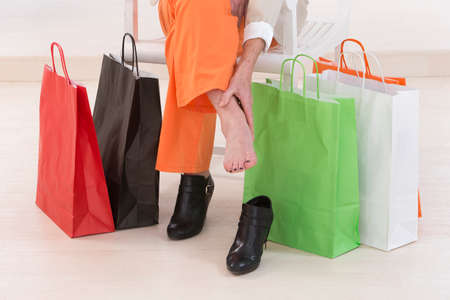senior woman sitting on a chair surrounded by shopping bags and rubbing her sore feet.の写真素材