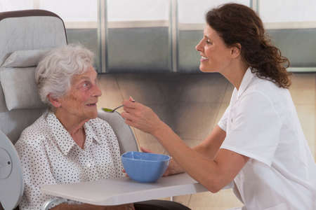 old woman in a wheel chair being fed in a retirement home setting.の写真素材