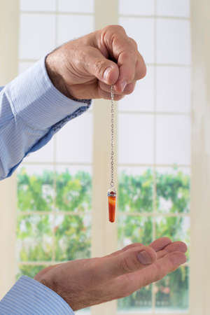 Hand with pendulum tool for dowsing.の写真素材