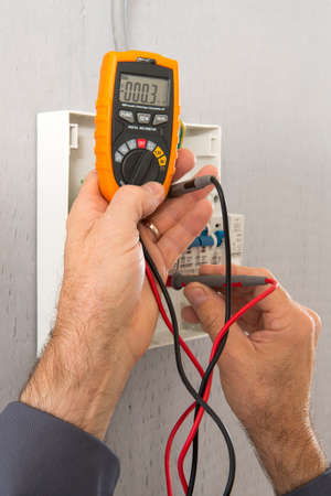 Hand of an electrician with multimeter probe at an electrical switchgear