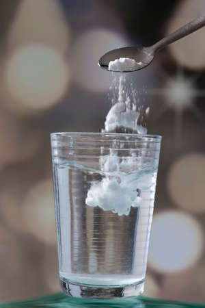 Spoon of baking soda falling in glass of waterの写真素材