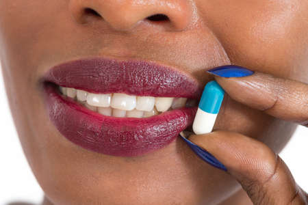 Woman taking pills. Close up of mouth and tabletの写真素材