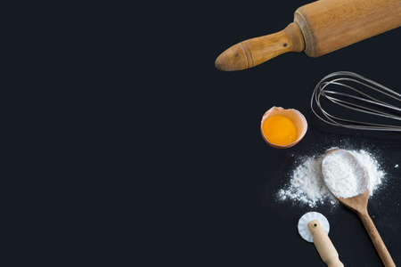 Rolling pin, whisk, flour and eggs on black backgroundの写真素材