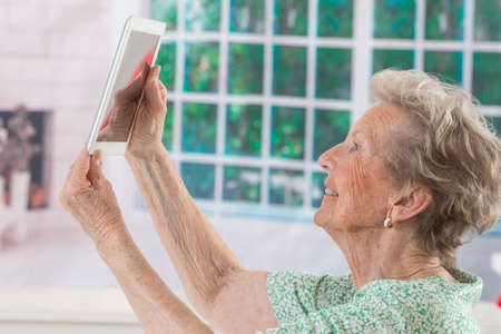 senior woman taking photo with tablet together at homeの写真素材