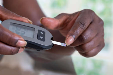 Woman checking blood sugar level by glucometer and test stripe at homeの写真素材