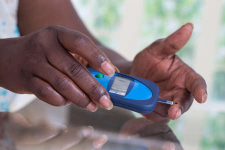 Woman checking blood sugar level by glucometer and test stripe at homeの写真素材