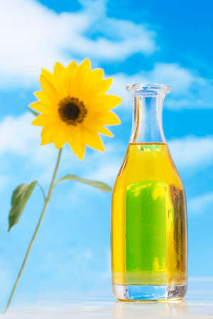 Bottle of oil and t sunflowers on blue skyの写真素材