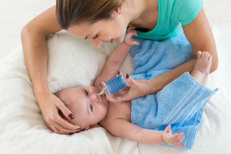 Mother cleaning mucus of baby nose with a nasal aspirator