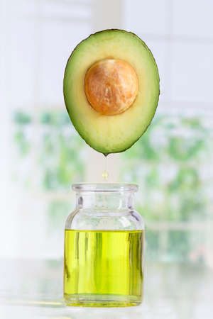 Fresh avocado and oil falling in a bottle on white