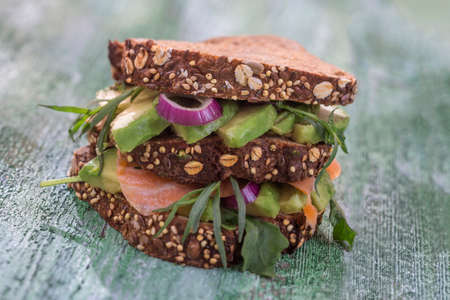 Countrybread Avocado, salted salmon sandwich with fresh herds on green craked paintt wooden board background. Healthy eating themeの写真素材