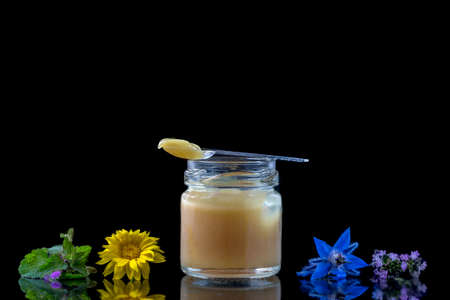 raw organic royal jelly in a small bottle with litte spoon on black surrounded by flowersの写真素材