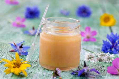 raw organic royal jelly in a small bottle with litte spoon on small bottle surrounded by flowersの写真素材
