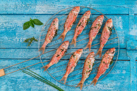 Plenty of red mullet fish ready to grill at barbecueon a blue wooden booard