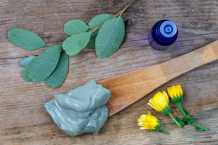 Composition with cosmetic clay and flowers and branch of eucalyptus, for spa treatments, in wood spoon on old wooden backgroundの写真素材