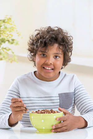Cute boy eating cereals for breakfast in the kitchen background