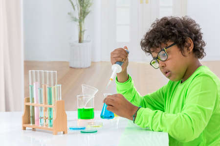 Cute young boy wearing green T-shirt doing science experiment with test tube in white background