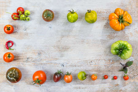 Frame of Various different color organic homegrown tomatoes on old wooden painted background. Background with red, yellow, orange and green tomatoes. Healthy vegetarian food concept. Copy space. Top viewの写真素材