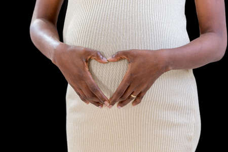 belly of pregnant, woman holding her hands in a heart shape on her baby bump with fingers, close upの写真素材