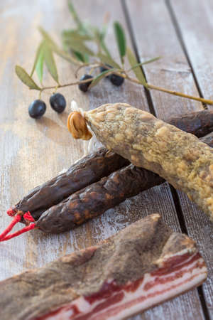 several variety of traditional Corsican charcuterie with an olive branch and black olives on wooden backgroundの写真素材