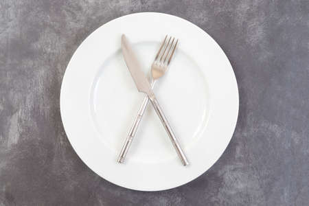 White plate, crossed fork and knife top view on gray plastic textured table surfaceの写真素材