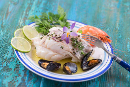 Cod fish fillet, Atlantic cod with seafood mussells,shrimps,lime and vegetable, on blue wooden...