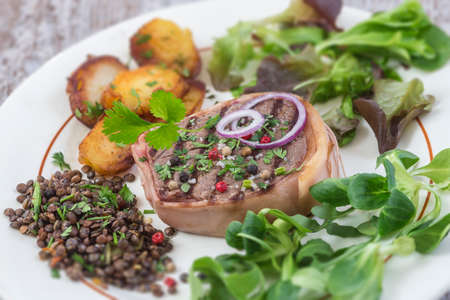 Beef tournedos and roquefort sauce with roasted potatoes and salad ans lentils on awhite plate grey...