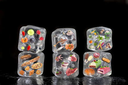 Concept of frozen products: fruits, vegetables, fishs, meat, spices herbs, pastry, were frozen inside ice cubes on black backgroundの写真素材