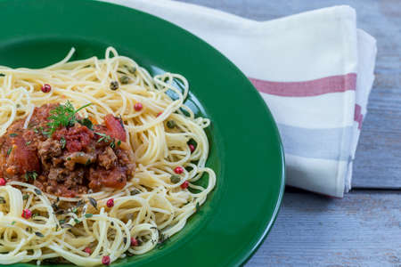 Green plate of Traditional Italian spahgetti Bolognaise or Bolognese with cooked pasta noodles topped with a tomato based meat sauce garnished with fresh basilの写真素材
