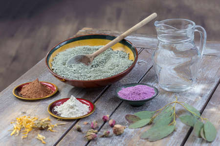 Composition of ceramic bowls of sea clay powder: red, pink, green ,purple ,pitcher of water, dryflowers, eucaliptus, concept of facial and body treatmenton wooden board, on vintage wall backgroundの写真素材