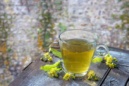 Healthy herbal linden tea with fresh linden flowers on wooden table Cup of organic linden tea, herbal drink with old flint wall backgroundの写真素材