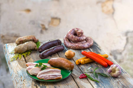 Selection of French Raw sausage with arugula leaves in a wooden board,vegetable on the table on old white cracked wall background.の写真素材