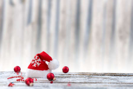 Christmas background with christmas ball, gift, red hat and snow on a wood board,over white old wooden wallの写真素材