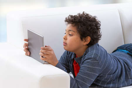 Young teenage boy using a tablet pc as he relaxes on his bed watching something on a mobile tablet...