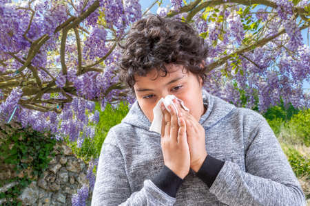 Pollen Allergy. Danger, Tennage boy sneezing in a flowers meadow. Concept: seasonal allergy.の写真素材