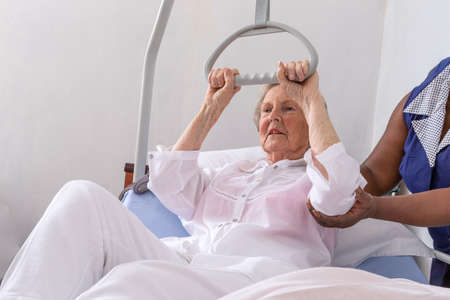 Nurse helps a patient to get up in hospital :nurse helping senior woman get up with credenceの写真素材