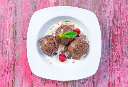 Chocolate ice cream balls with mint and raspberry close up and copy space on pink woodenの写真素材