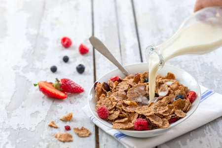 Healthy cereal breakfast. with Berries - fresh strawberries and blueberries, with milk pourring on old wooden tableの写真素材