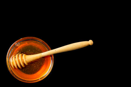 Honey in bowl with wood stick isolated on black backgroundの写真素材