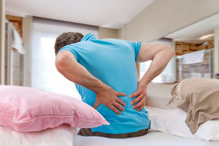 Senior male suffering sharp back pain, sick person getting up from bed, after rest
