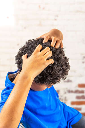 Sad young boy scratching hair for head lice or allergiesの写真素材