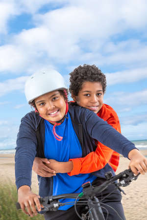 10 and 12 years old boys riding a bicycle. over a beach backgroundの写真素材