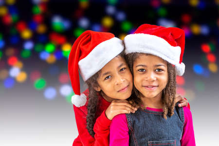 Happy little girls on Santa hats against blurred festive bokeh lights. Christmas celebrationの写真素材