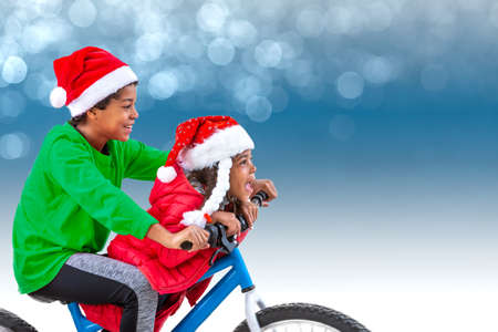 Christmas image of a boy and girl, riding his bicycle wearing Santas hat, over a blue light bokeh.の写真素材