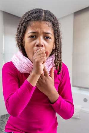 A young girl coughing, against interior backgroundの写真素材