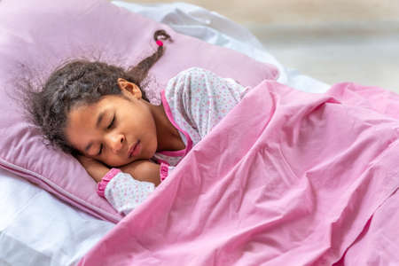 Beautiful girl is wear a pajamas and pink environment lying in bed. Close-up portrait of sleeping pre-teen girl. Child portrait in pastel tones. Top view.の写真素材