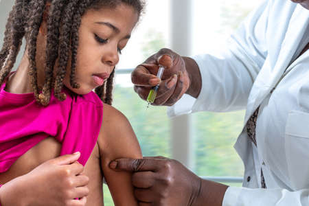 little girl looking at her arm, while receiving vaccine at hospitalの写真素材