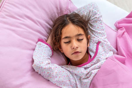 Beautiful girl is wear a pajamas and pink environment lying in bed. Close-up portrait of sleeping pre-teen girl. Child portrait in pastel tones. Top view.の写真素材