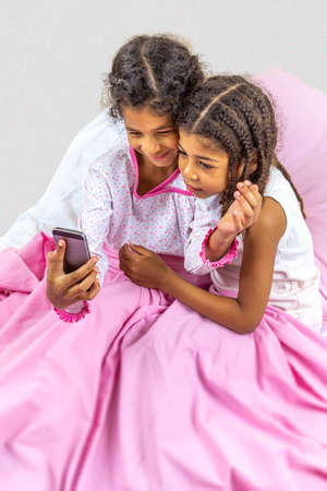Little girls using digital tablet and smartphone playing in bed. with pink linenの写真素材