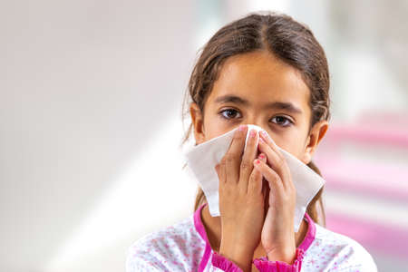 Cute young girl child sneezing in a tissue blowing his runny nose. having fluの写真素材